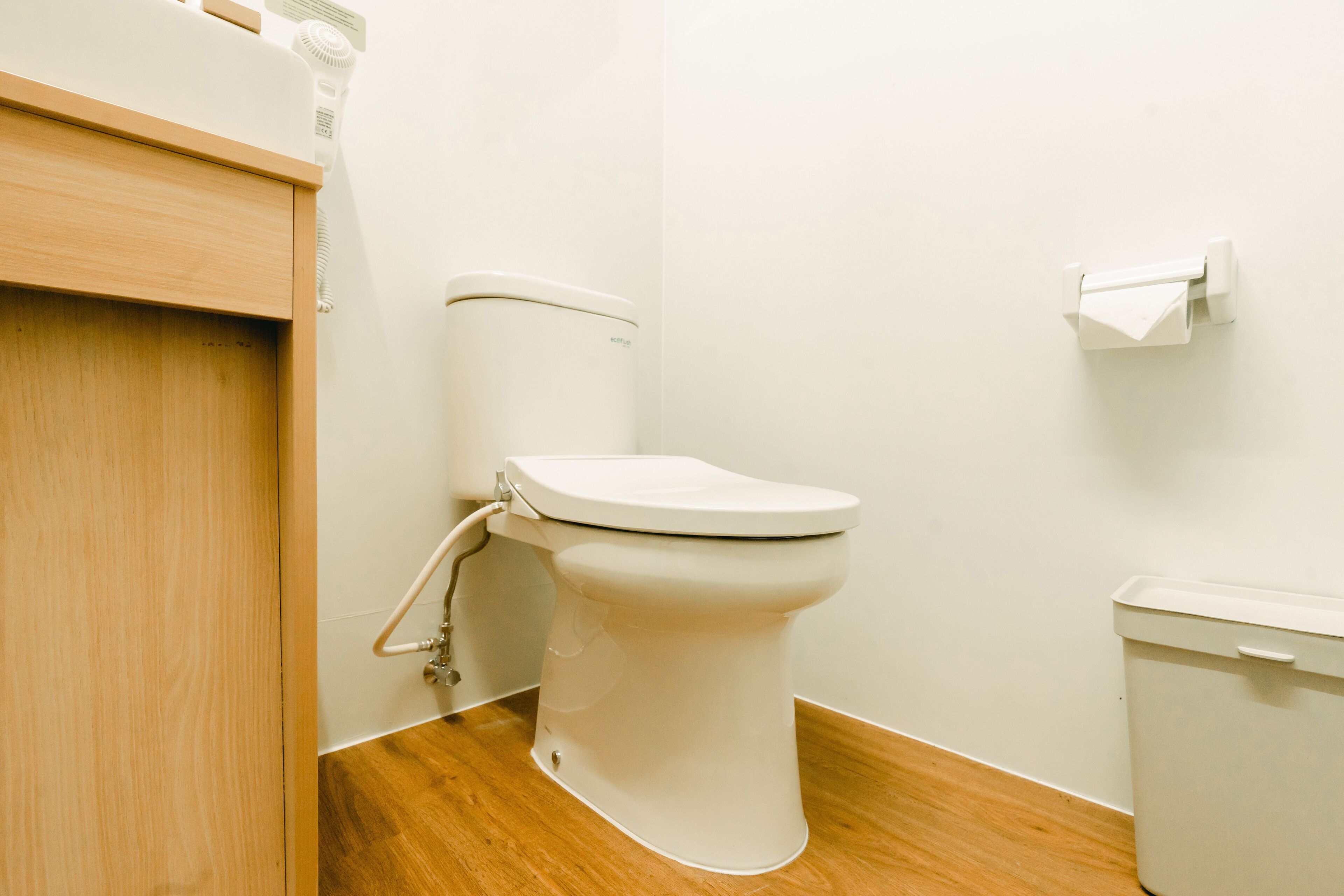 Inodoro blanco con tanque, suelo de madera y pared blanca.