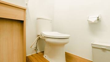 Inodoro blanco con tanque, suelo de madera y pared blanca.