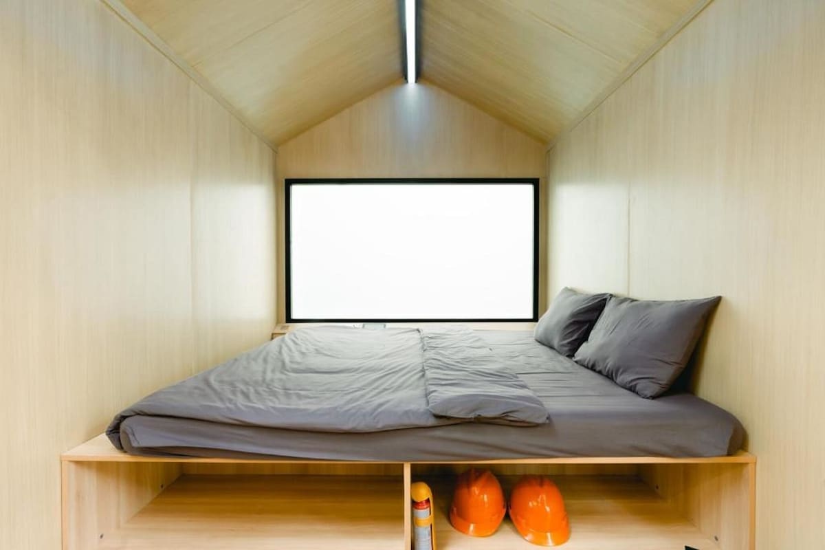 Een kleine kamer met een bed, een groot raam en een plank met helmen.