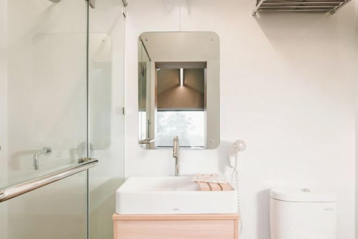 Un baño moderno con cabina de ducha de vidrio, un lavabo blanco con tocador de madera y un espejo sobre el lavabo.