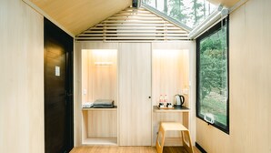 Habitació petita amb interior de fusta, finestra que donava a arbres, un tamboret i una taula amb una paperera i ampolles.