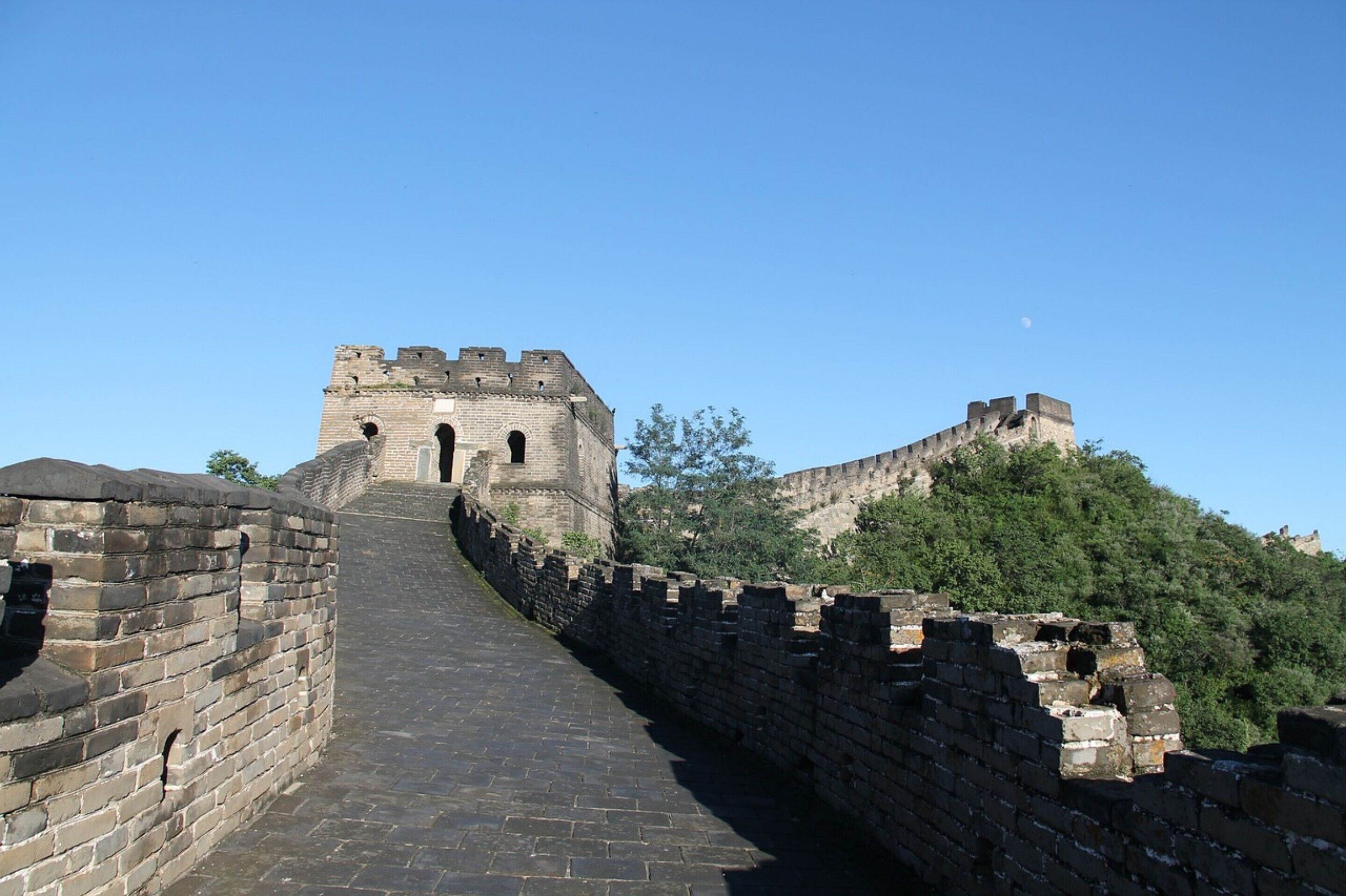 Une portion de la Grande Muraille de Chine, avec un ciel dégagé et la lune en arrière-plan.