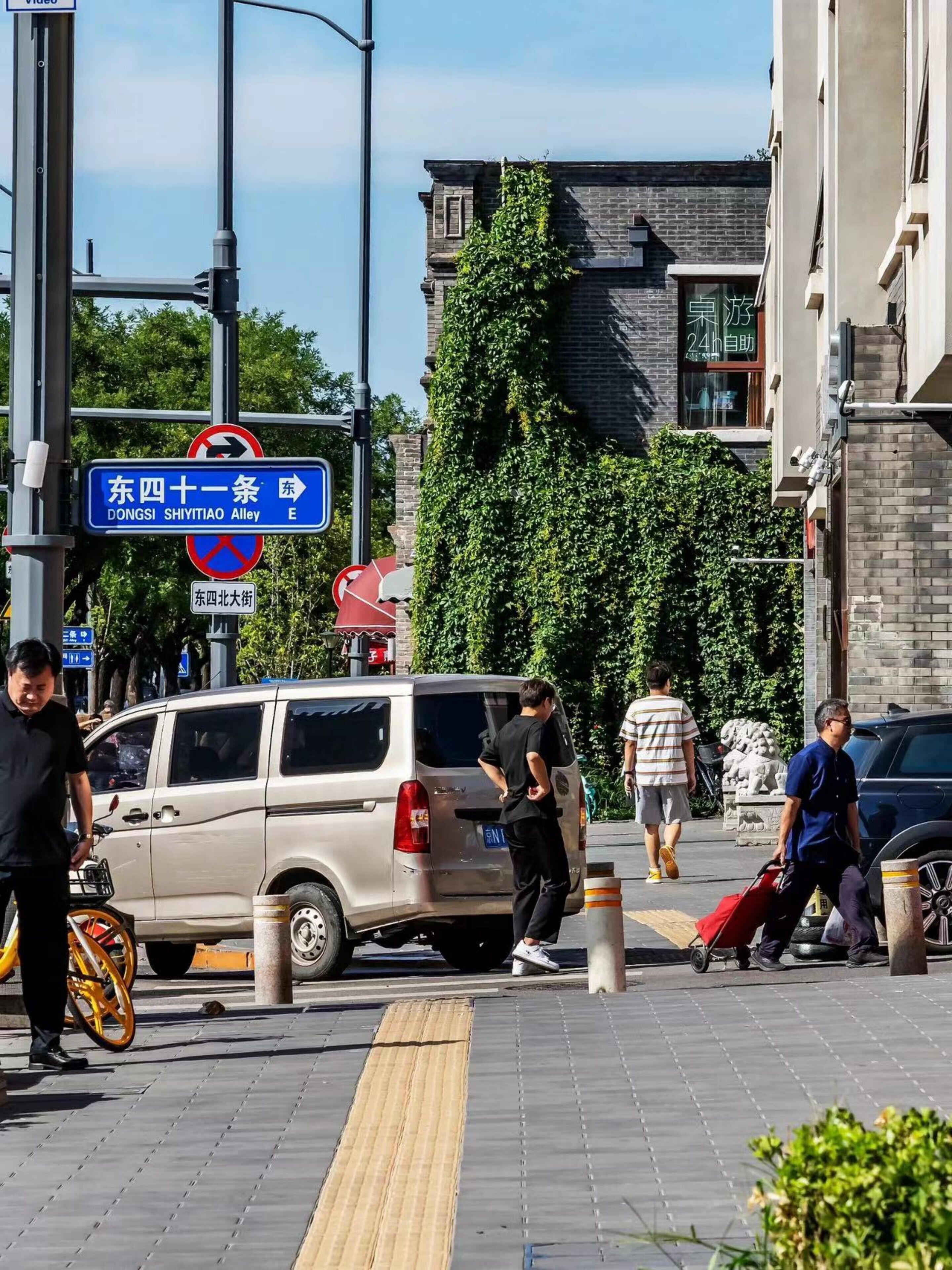 Une scène de rue avec un fourgon garé sur le bord, un panneau de signalisation bleu et un bâtiment à la façade en briques.