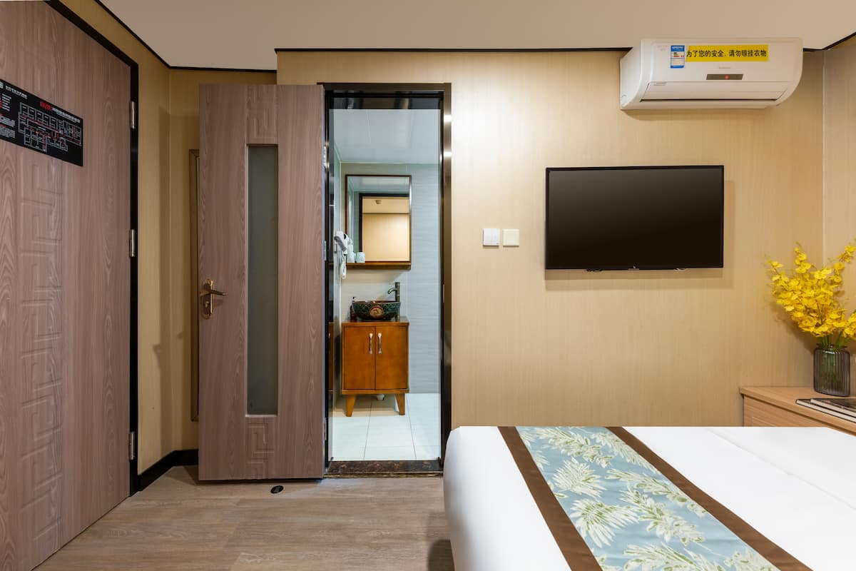 Une chambre d’hôtel comprenant un lit, un téléviseur fixé au mur, une armoire en bois et une porte donnant accès à une salle de bain.