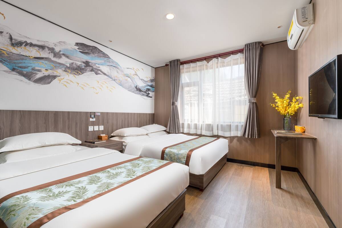 Une chambre d’hôtel avec deux lits, un grand tableau au mur, une télévision et une petite table sur laquelle est posé un vase de fleurs.