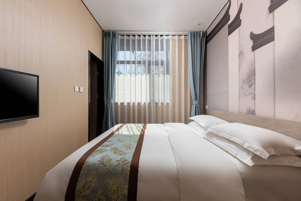 Une chambre d’hôtel avec un lit, un téléviseur à écran plat fixé au mur et une fenêtre avec des rideaux légers.