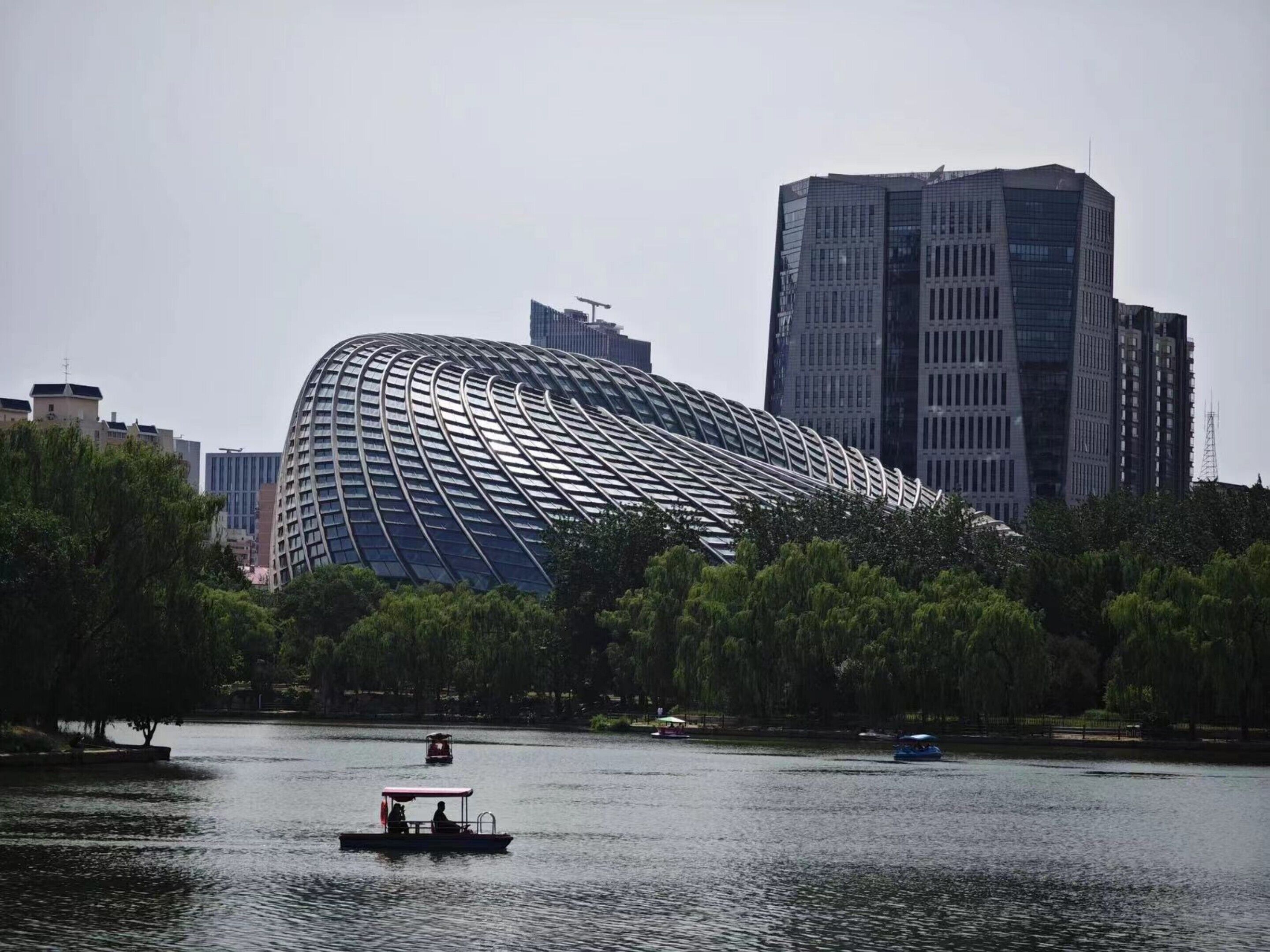 Un edificio moderno con un techo curvo distintivo, rodeado de árboles y agua.