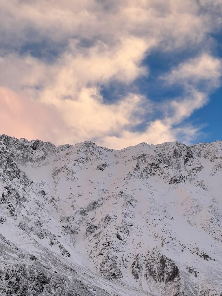 Cordillera nevada con terreno accidentado y cielo parcialmente nublado.