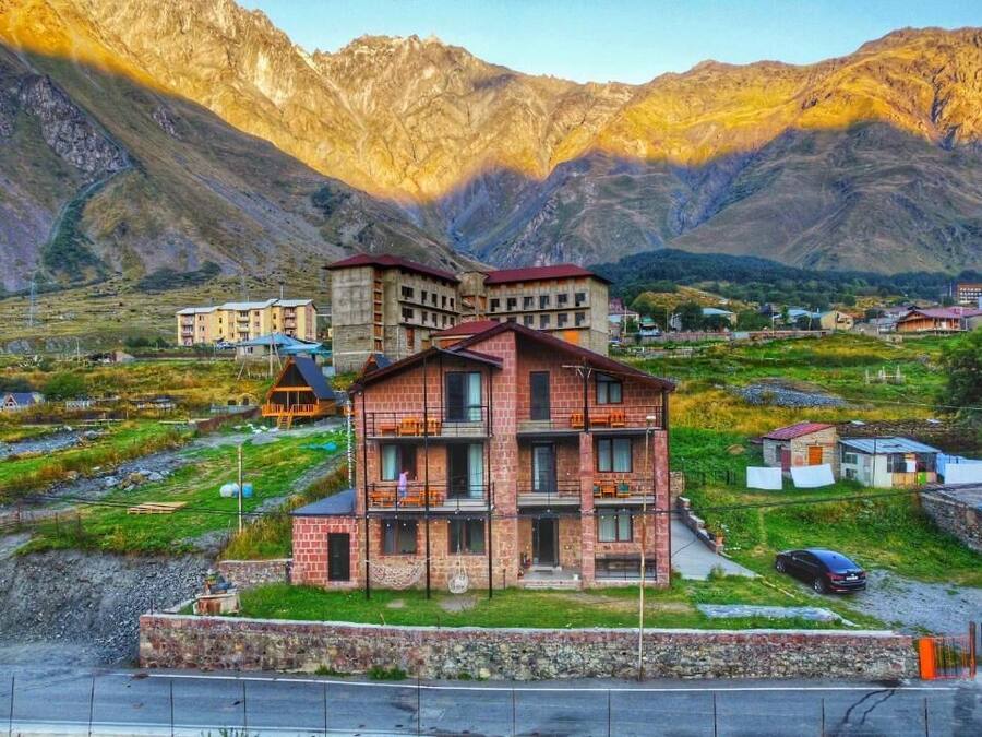 A multi-story building with balconies, surrounded by a mountainous landscape.