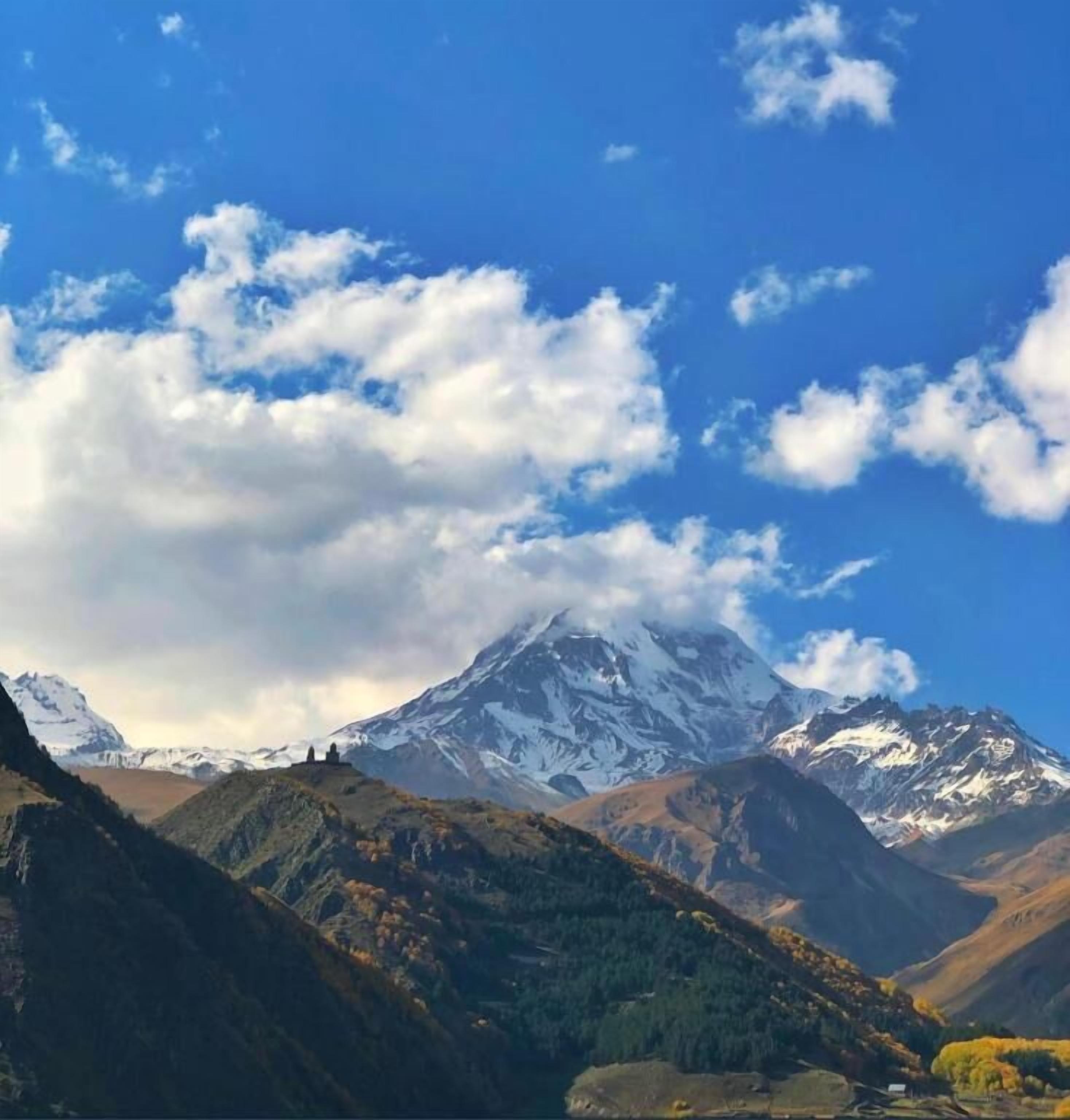 A mountain landscape with snow-capped peaks and a clear blue sky.