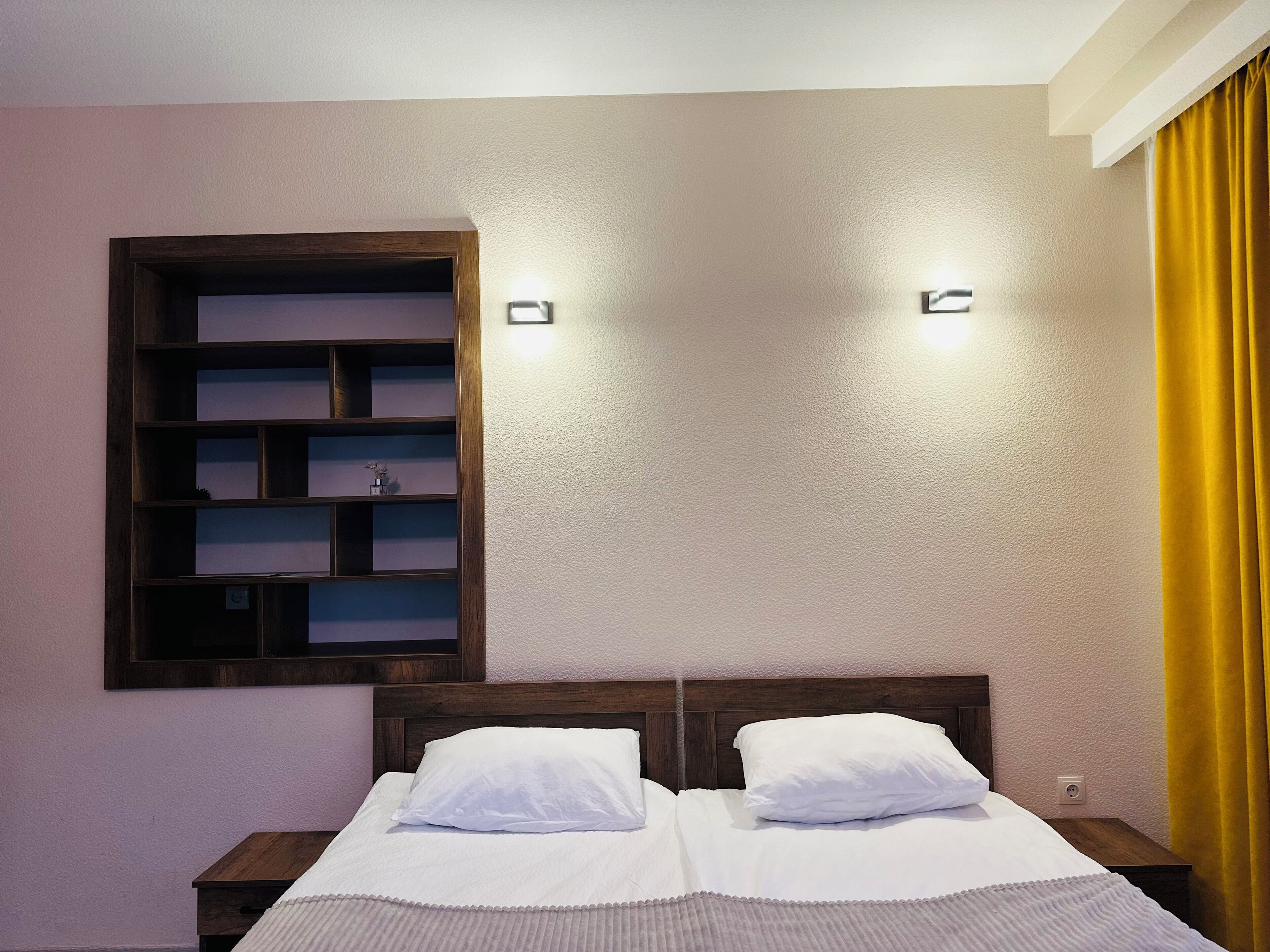 Una cama bien tendida con sábanas blancas, un cabecero de madera y una estantería con varios compartimentos contra la pared.
