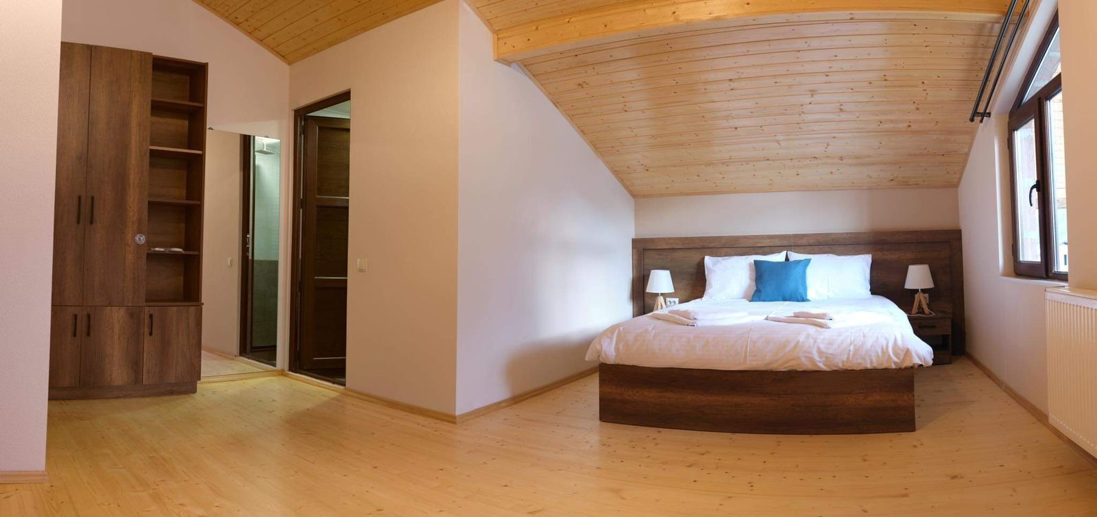 Une chambre avec un plafond en bois, un grand lit avec une literie blanche et des oreillers bleus, une armoire en bois et un dressing.