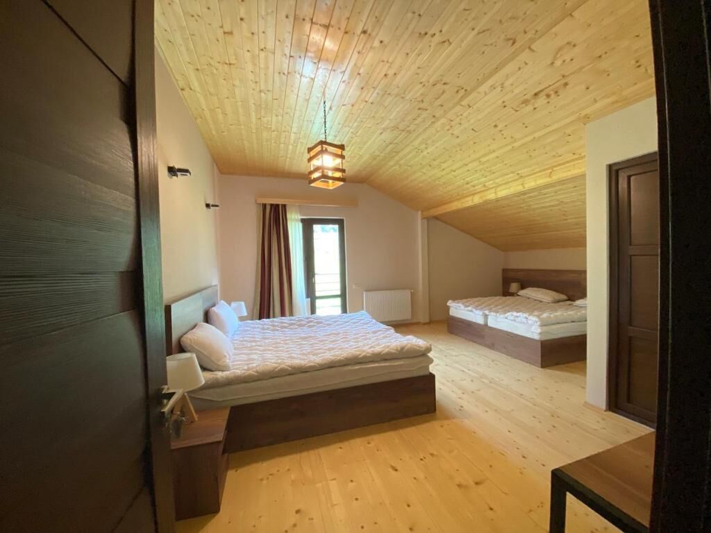 A bedroom with a sloped ceiling, a large bed, a smaller bed, and a window with curtains.