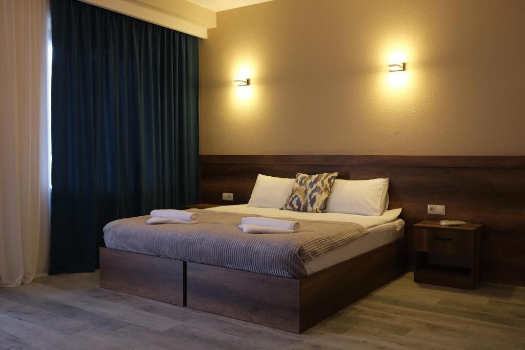 A hotel room with a large bed, two wall-mounted lights, a nightstand, and a dark curtain.