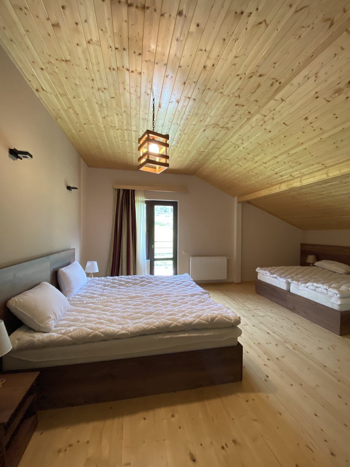 Une chambre avec un plafond en bois, un lit doté d’un matelas matelassé, une table de chevet et une lampe.