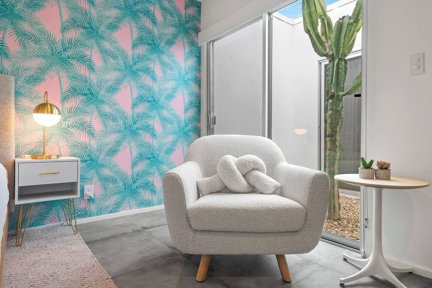 A modern living room with a grey armchair, a small side table with a lamp, and a cactus plant.