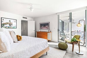 Une chambre moderne avec un lit, une commode, un téléviseur et un balcon équipé de chaises.