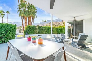 Une terrasse extérieure avec une table et des chaises blanches, des plantes en pot et une vue sur les montagnes.