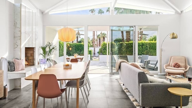 Una sala de estar moderna con comedor, ventanas amplias y vistas a un jardín.