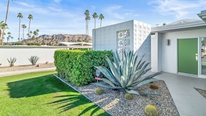 Una casa moderna con un césped bien cuidado, una planta de agave grande y un jardín de estilo desértico.