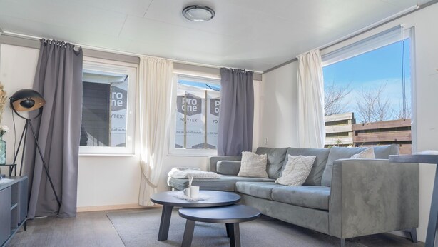 A modern living room with a grey sofa, two round tables, and a large window with curtains. - Modern chalet on the Wadden Sea, near the beach (Westerland)