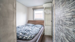 A bedroom with a bed, a window, a wardrobe, and a stone-textured wall. - Modern chalet on the Wadden Sea, near the beach (Westerland)