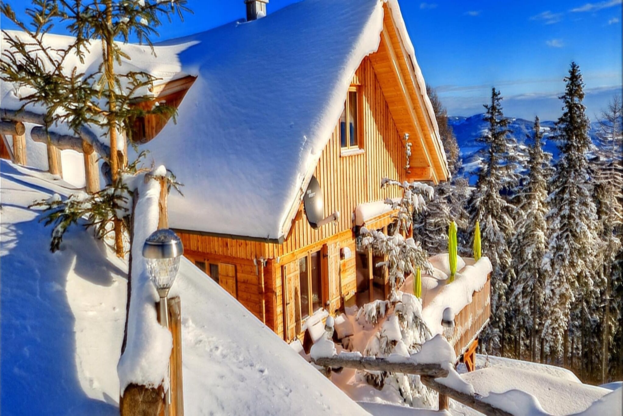 Un chalet en bois, dont le toit est recouvert de neige, entouré d’arbres et de montagnes enneigés.