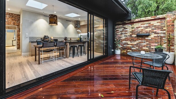 A modern kitchen with a large window, a dining area with a table and chairs, and a brick wall. - North Fremantle Cottage (North Fremantle)