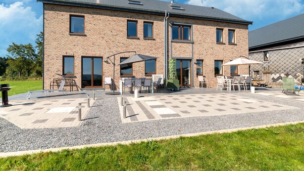 Ein zweistöckiges Backsteingebäude mit einer Terrasse, die Sitzgelegenheiten im Freien und eine Pergola bietet.
