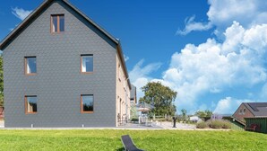 Ein modernes Gebäude mit grauer Fassade und geneigtem Dach, ausgestattet mit zahlreichen Fenstern und einem gepflegten Rasen davor.