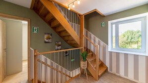 Eine Holztreppe mit Geländer, einem Blumentopf und einem Fenster mit Blick auf Bäume.