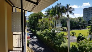 A balcony with a view of a street, greenery, and a building in the background. - Bobato Appartement A (Curepipe)