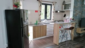 A compact kitchen with a refrigerator, a sink, and a window with curtains. - Bobato Appartement A (Curepipe)