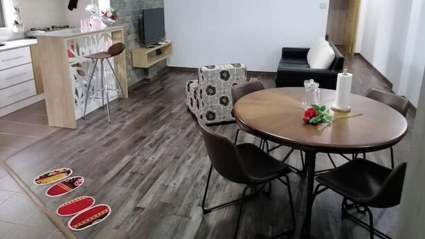 A modern kitchen with a built-in stove, a dining area with a round table and four chairs, and a seating area with a sofa and a TV. - Bobato Appartement A (Curepipe)