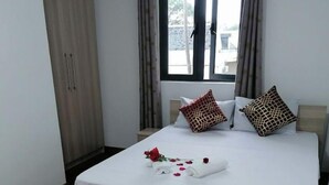 A neatly made bed with a white mattress, two patterned pillows, and a rose arrangement on the bedspread. - Bobato Appartement A (Curepipe)