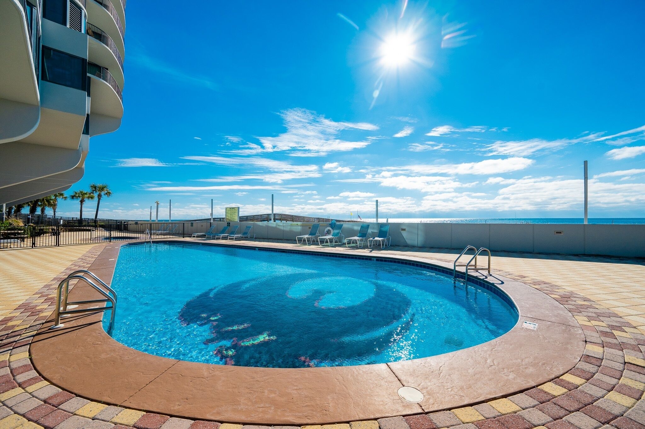 A swimming pool with a circular design, surrounded by a tiled deck, and a view of the ocean.
