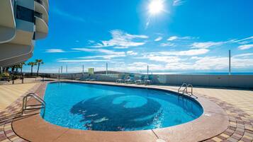 A swimming pool with a circular design, surrounded by a tiled deck, and a view of the ocean.