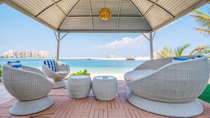 A covered outdoor seating area with wicker furniture and a view of the beach and ocean. - 5BR Beach & pool villa in Palm (Dubai)