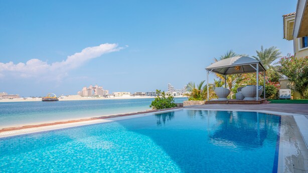 A swimming pool with a view of a beach and hotel buildings in the background. - 5BR Beach & pool villa in Palm (Dubai)
