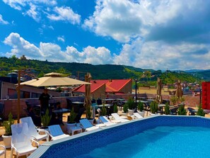Ein Poolbereich auf dem Dach mit Liegestühlen, Sonnenschirmen und Blick auf Stadt und Berge.