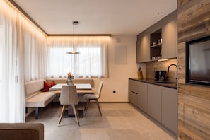 Uma cozinha moderna com eletrodomésticos embutidos, um espaço de refeições com banco e mesa, e uma janela grande com cortinas.