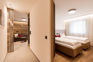 Quarto de hotel moderno com chão de madeira, um sofá, uma cama e um detalhe decorativo na parede.