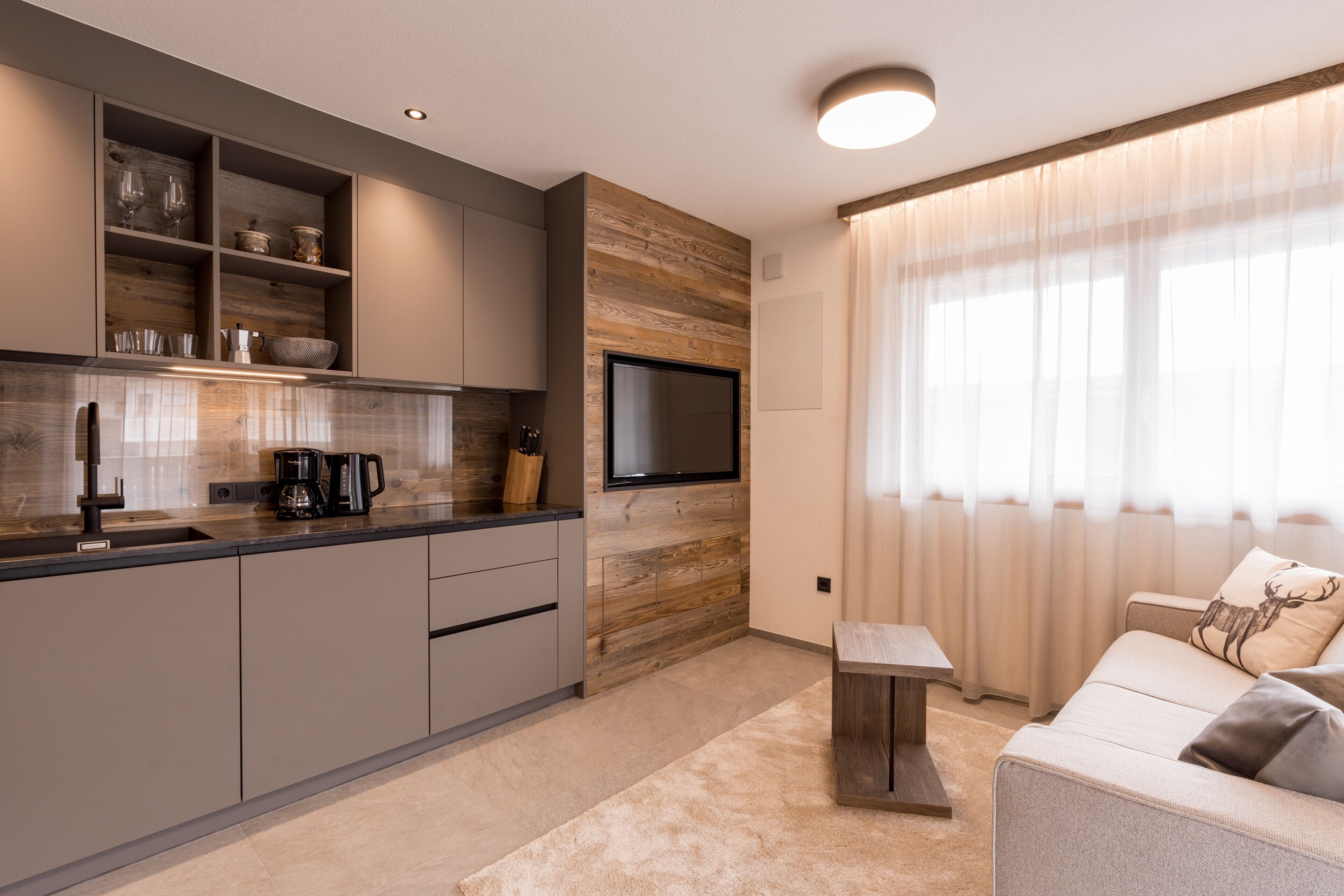 A modern kitchen with built-in appliances, a flat-screen TV, and a dining area with a sofa and table.