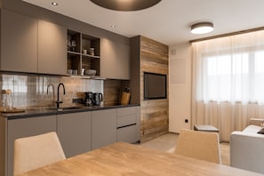 Una cucina moderna con mobili grigi, una parete d'accento in legno, una TV a incasso e un'area pranzo con tavolo e sedie.