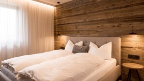 A modern bedroom with a wooden headboard, a large bed with white linens, a bedside table, and a hanging light fixture.