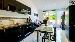 Une cuisine moderne avec des meubles noirs, un coin repas comprenant une table et des chaises, et une vue sur un jardin grâce à une porte vitrée.