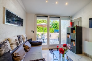 Ein modernes Wohnzimmer mit einer Couch, einem Bücherregal und Blick auf eine Terrasse.