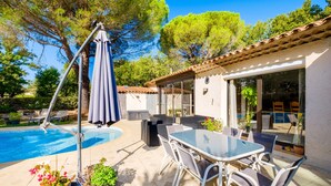 Un espace aménagé au bord de la piscine, avec une table et des chaises, un coin salon abrité et une vue sur la piscine.