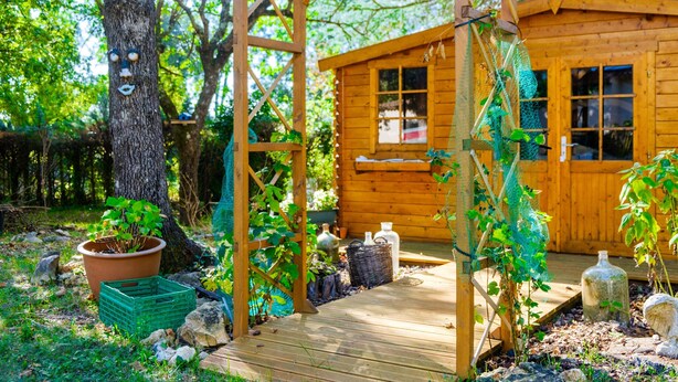 Une cabane en bois dotée d’une terrasse en bois, entourée d’arbres et de verdure.