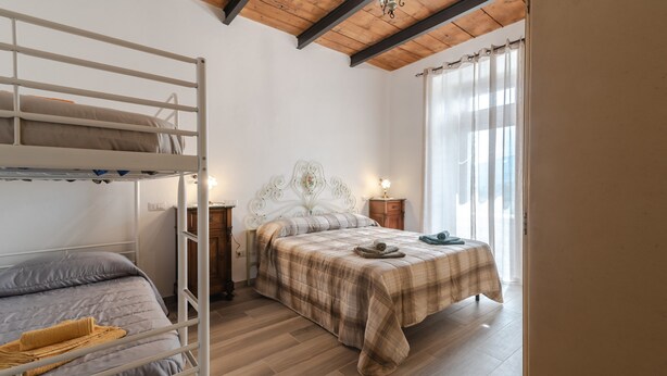 A bedroom with a bunk bed, a single bed, wooden flooring, a chandelier, a nightstand, and a window with curtains. - Holiday Home 'Casa Pifaro' in Monterchi (Monterchi)
